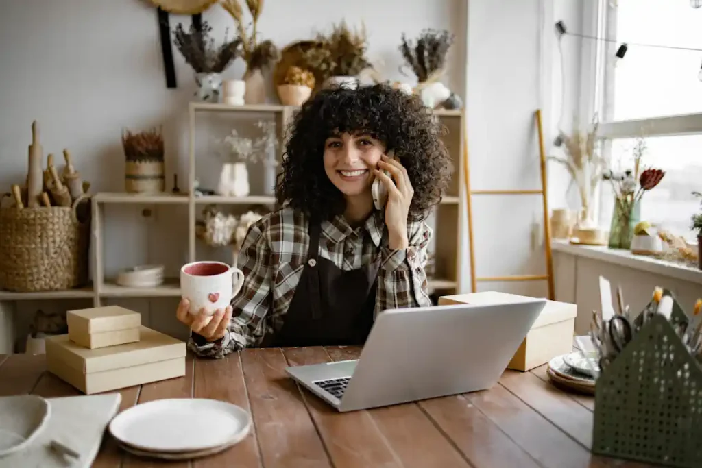 Une femme au téléphone devant son ordinateur en tenant une tasse dans sa main