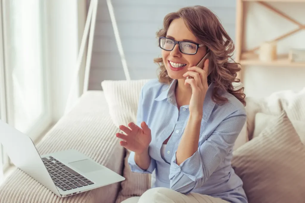 Une femme au téléphone devant son ordinateur posé sur le canapé