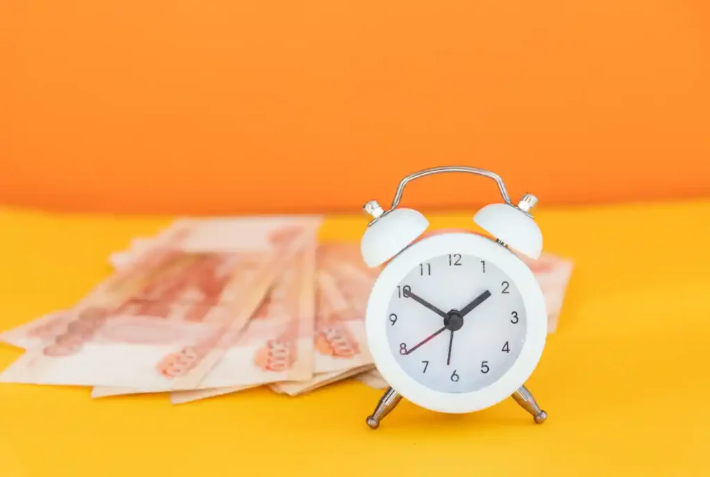 Un réveil posé à côté de quelques liasses de billets sur un fond jaune et orange