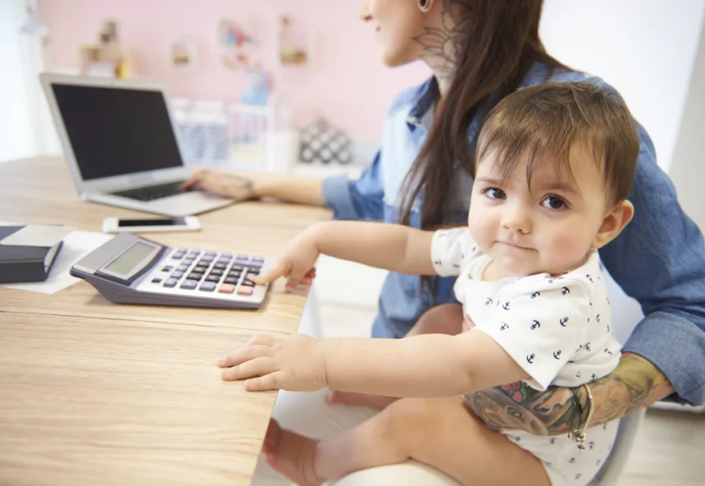 Une femme sur un ordinateur qui tient un bébé dans ses bras