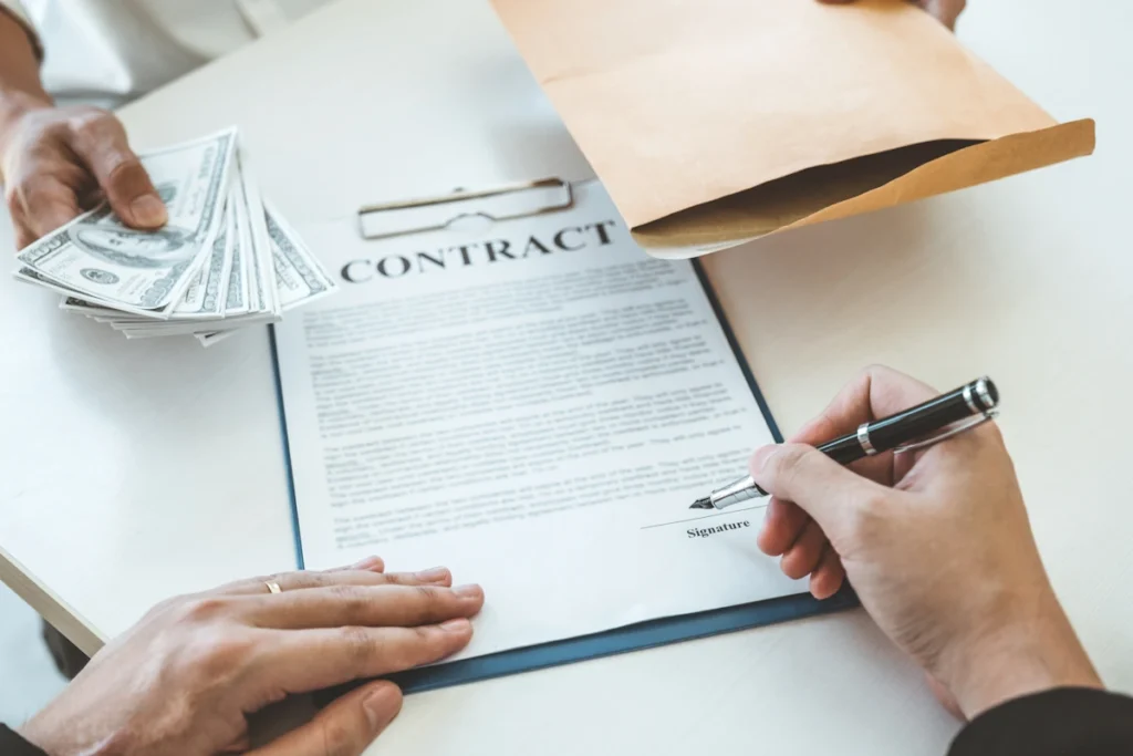 Un homme qui signe un contrat devant une autre personne qui tient une enveloppe et de l'argent
