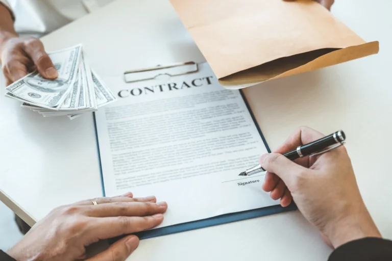 Un homme qui signe un contrat devant une autre personne qui tient une enveloppe et de l'argent