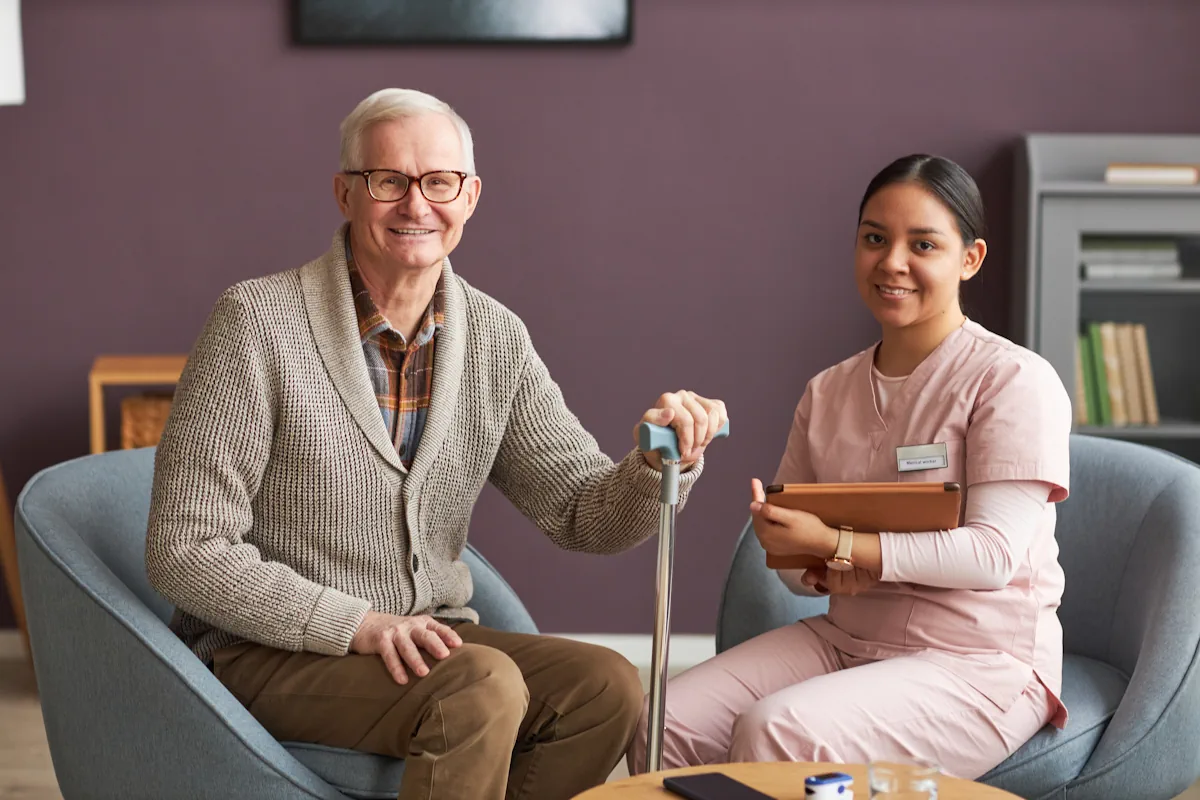 Une femme en blouse rose assise à côté d'un sénior avec une canne