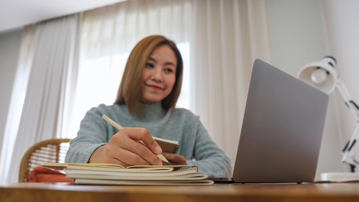 Une femme qui suit une formation sur son ordinateur en prenant des notes