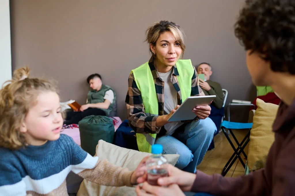 Une femme en gilet vert fluo qui tient un carnet dans sa main et qui discute avec une personne qui tient la main d'un enfant