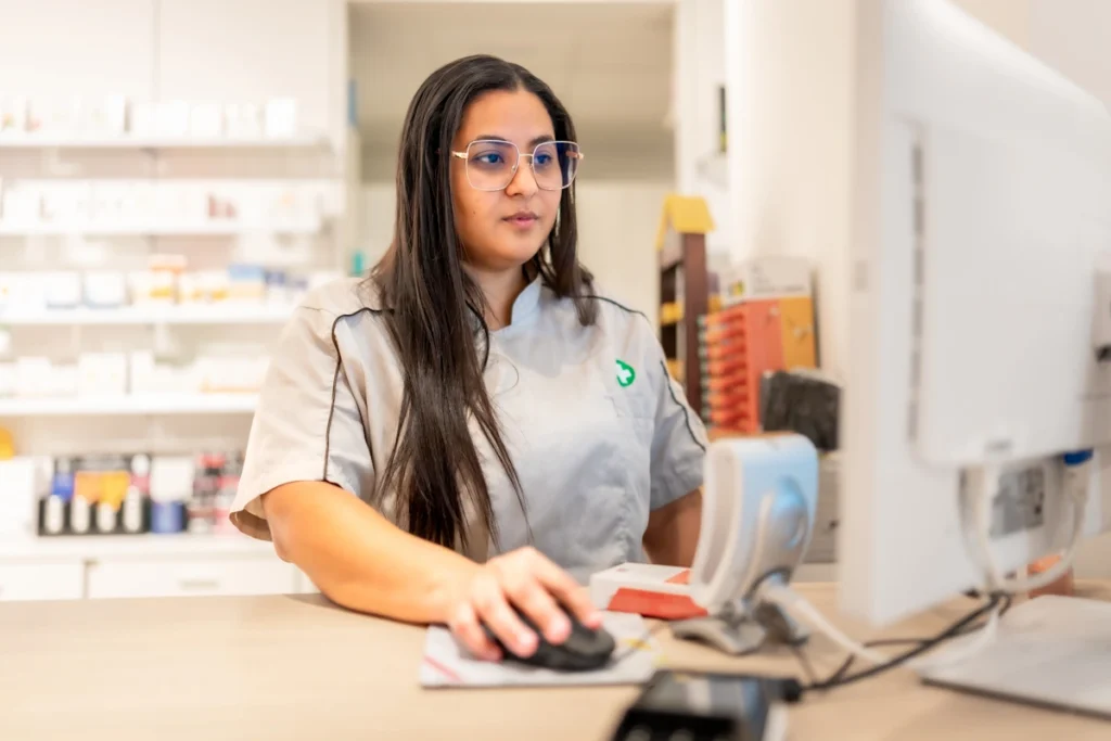 Une femme en blouse dans une pharmacie qui travaille devant un ordinateur
