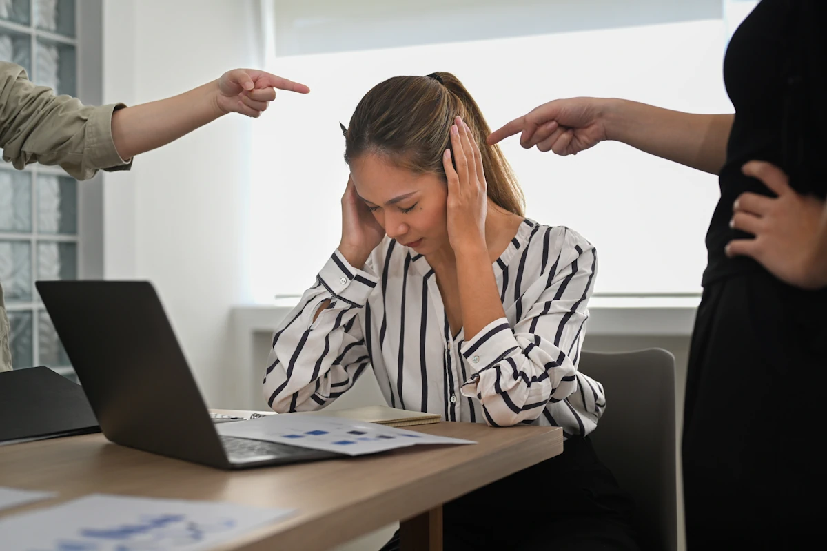 Une femme assise en se tenant la tête pour cacher ses oreilles et deux doigts qui pointent vers elle