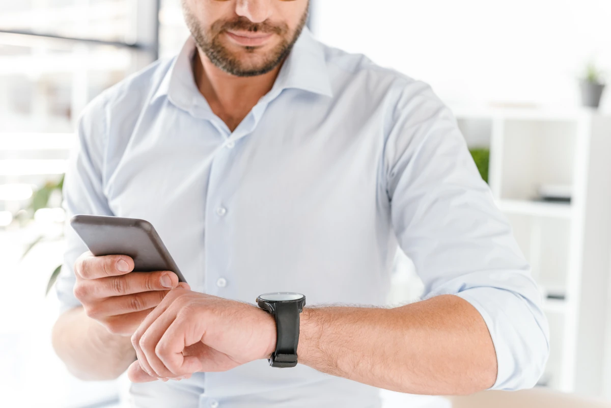 Un homme qui regarde sa montre en tenant un smartphone dans sa main
